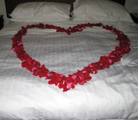 Red heart of rose petals on honeymoon bed.